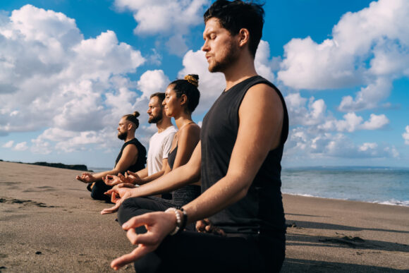 Male and female in tracksuit sitting in asana for seeking mindfulness and enlightenment during practice retreat, calm people enjoying relaxation and vitality during yoga training at seashore coastline