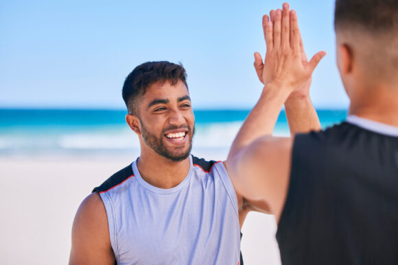 Happy man, high five and teamwork in fitness on beach for workout success, training or outdoor exer.
